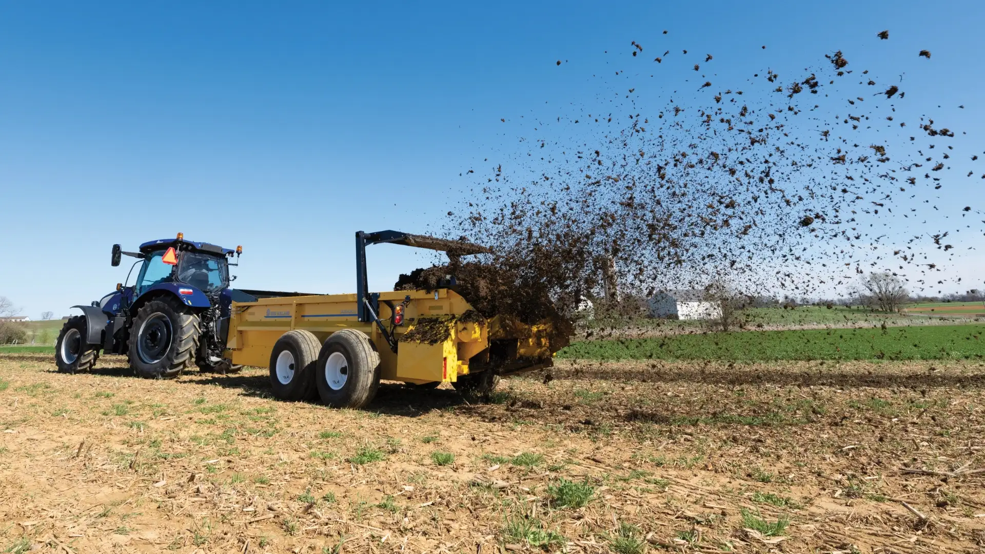 Manure sent flying through the air by a yellow box spreader.