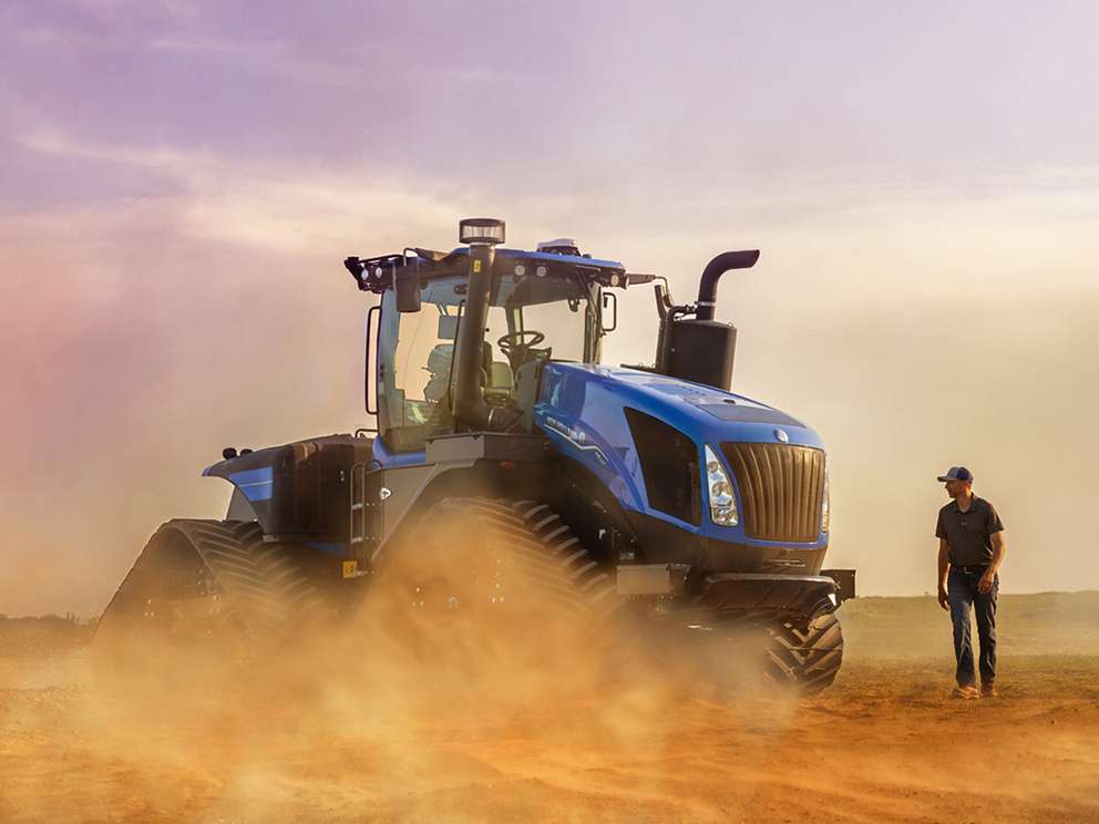 Blue New Holland T9 Smartrax sitting in field with person next to it with dust