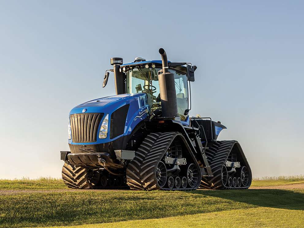 Blue New Holland T9 tractor sitting in field with sunset background