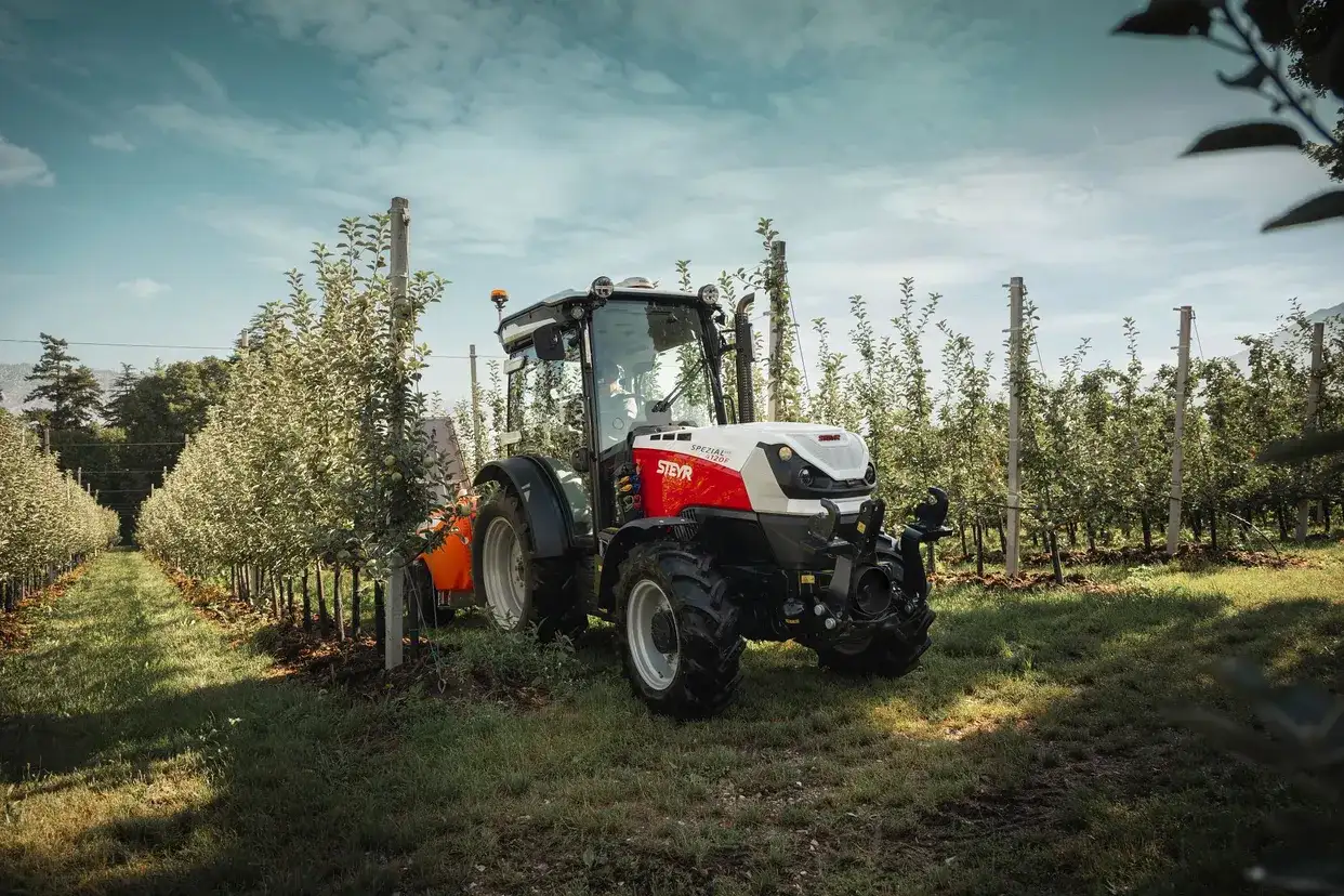 STEYR Spezial orchard tractor on a slope among apple trees with mountains behind
