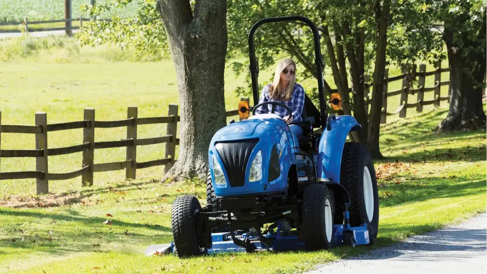 Woman drives Boomer tractor with mid mount mower attachment