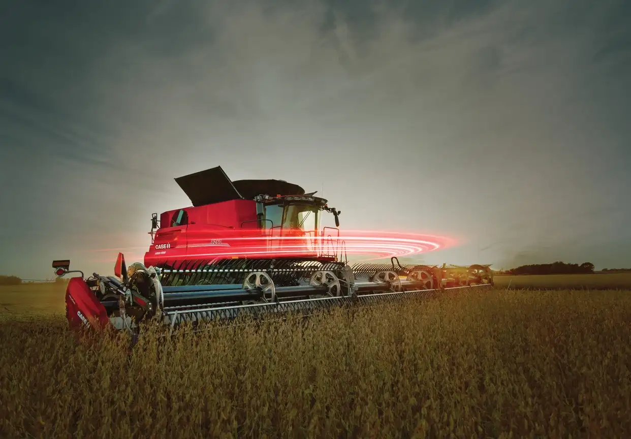 Red CASE IH combine harvester in a field at dusk with a swirling pink light effect around its middle.