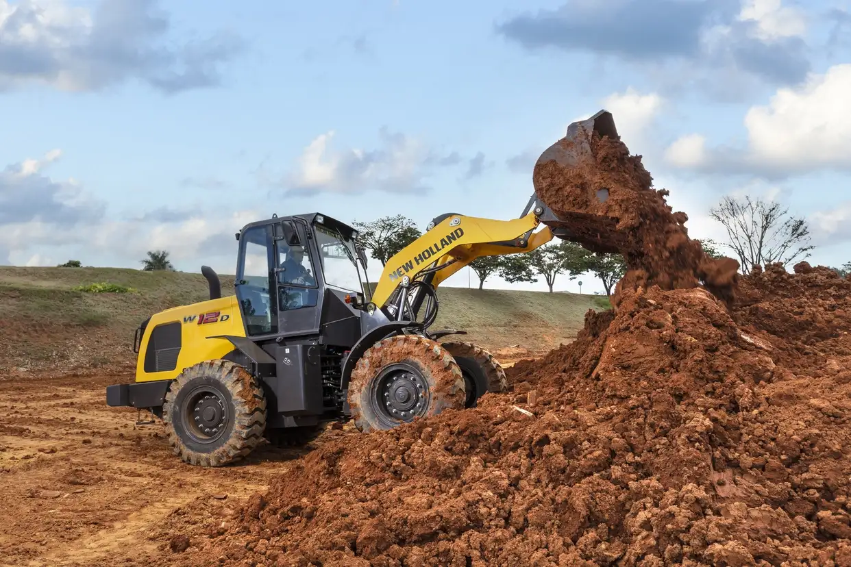 foto ao ar livre, da pá carregadeira New Holland Construction em operação, sobre a terra. 
