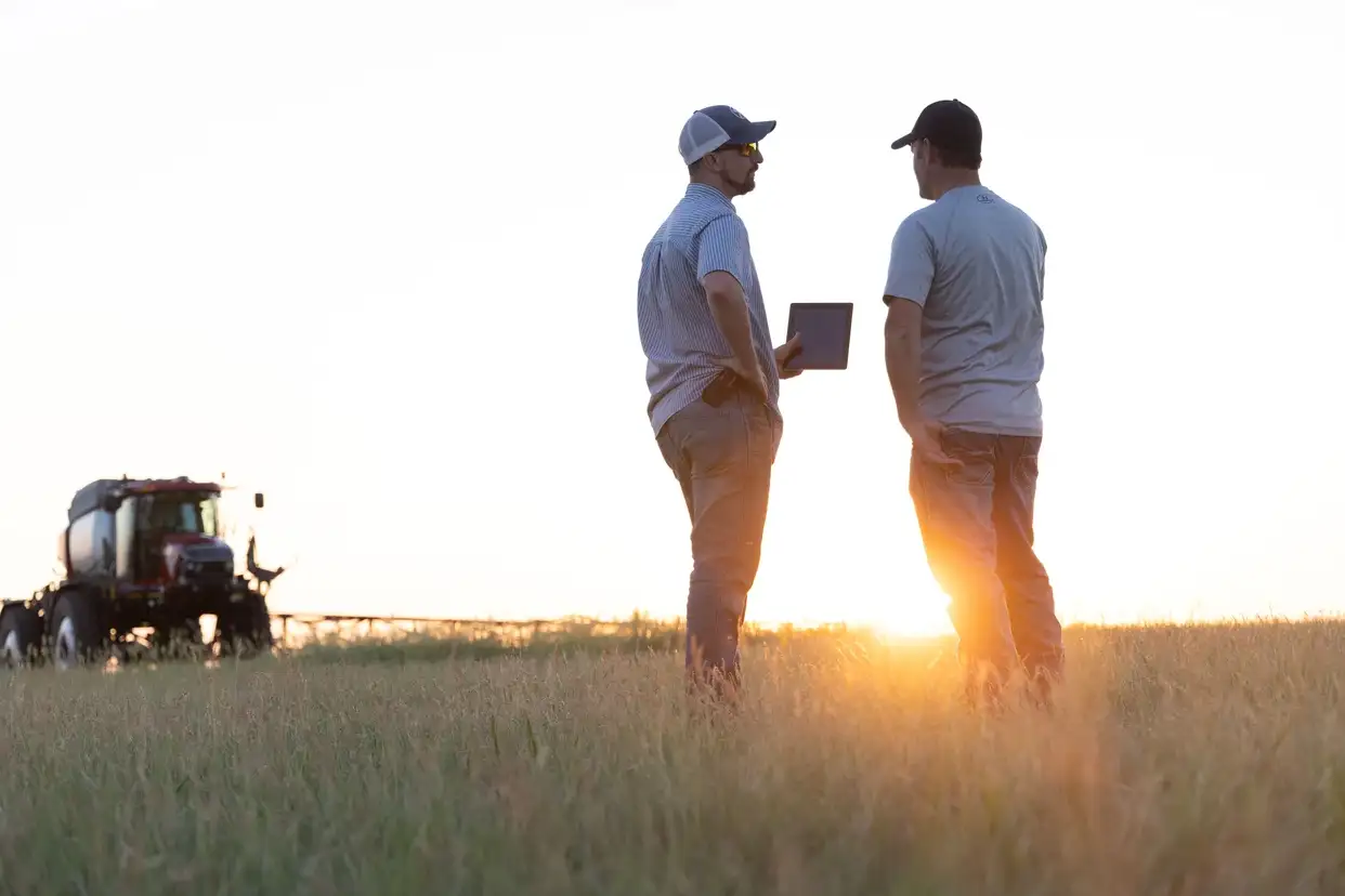 Two farmers standing in a field, one with tablet in hand, and Case IH farm equipment in front of them.