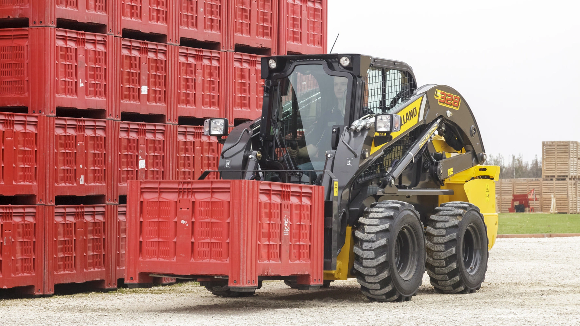 New Holland Skid Steer Loader stacking red crates outside a warehouse.