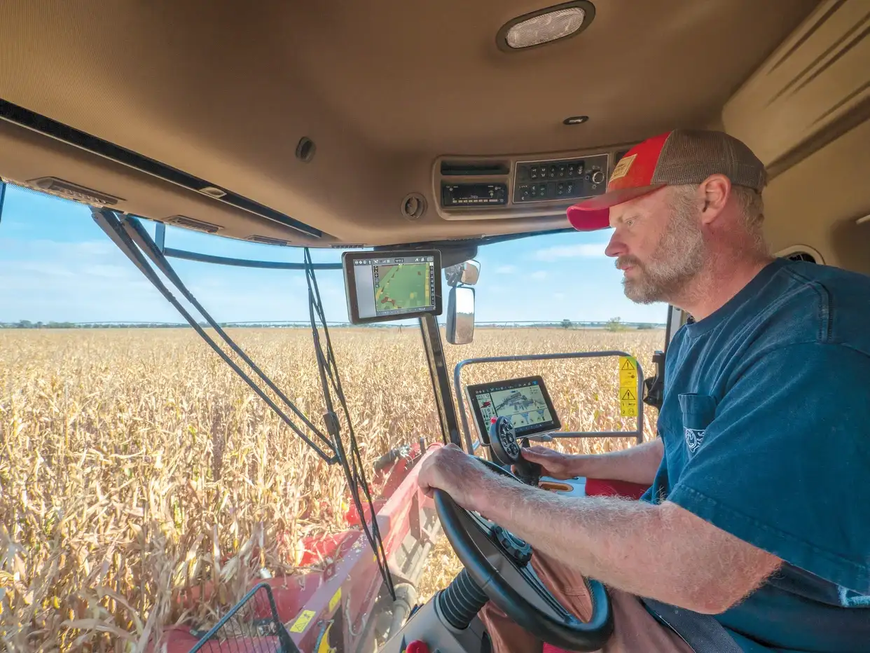 Farmer operating a modern Case IH combine harvester in a cornfield, using digital controls and navigation screens.