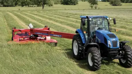 Blue tractor pulling disc mower conditioner in a field.