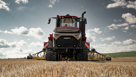 Front view of a Case IH Steiger 555 articulated tractor with a wide yellow implement in a stubble field under a cloudy sky.