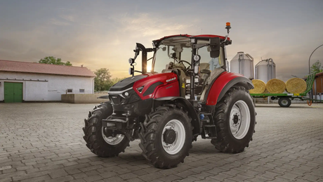 Red Case IH tractor in a farmyard with hay bales and silos in the background at sunset