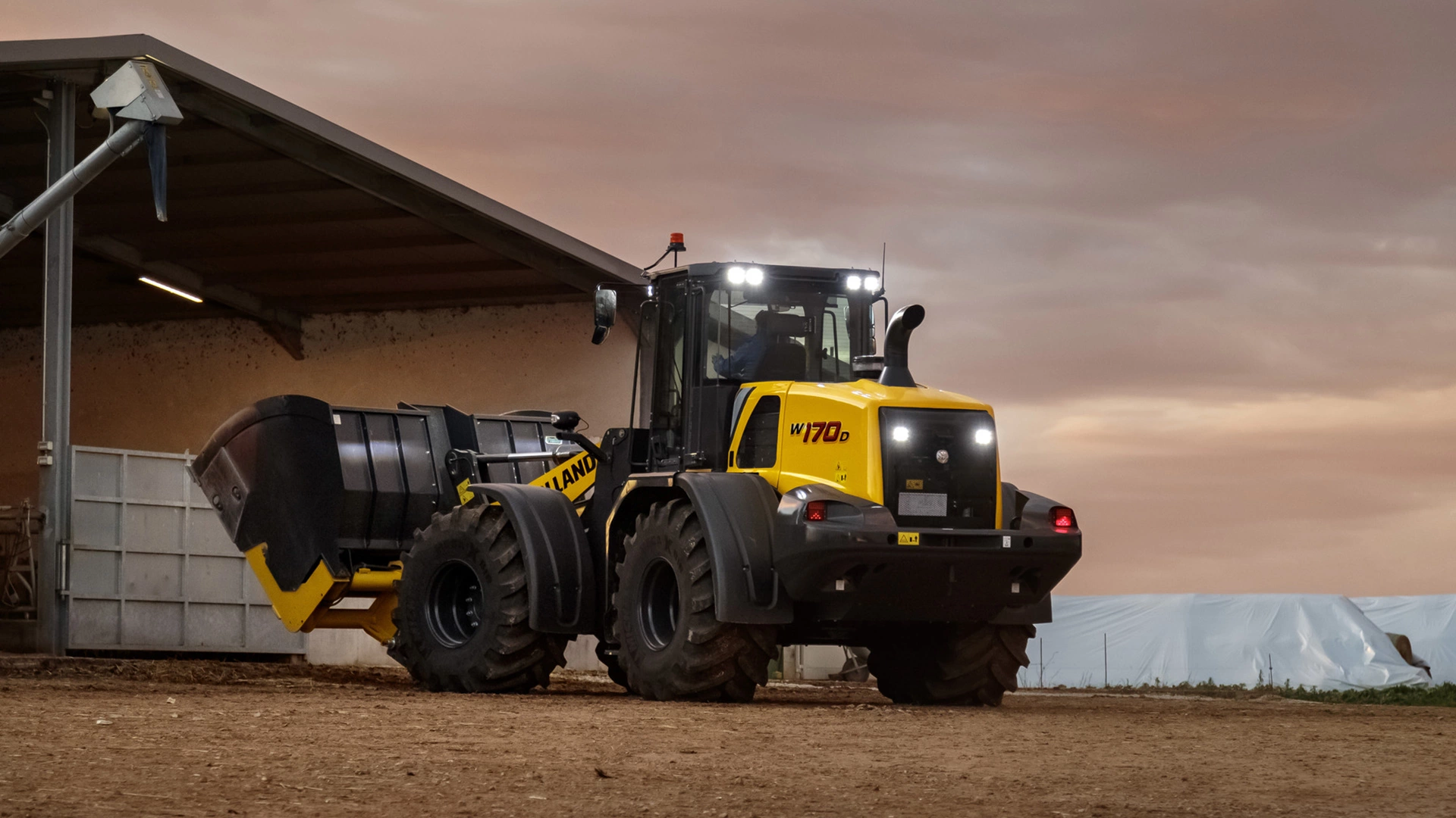 New Holland wheel loader with bucket attachment, ready for nighttime operations in farm setting.