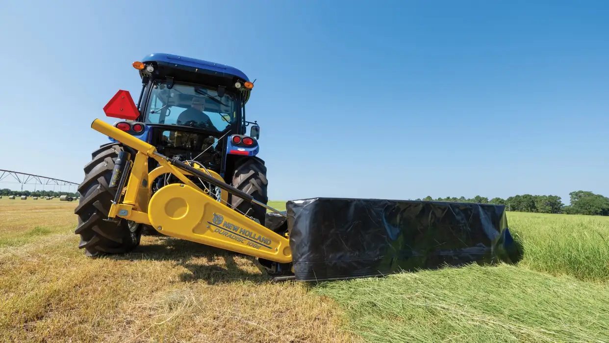 New Holland tractor pulling disc mower in field.