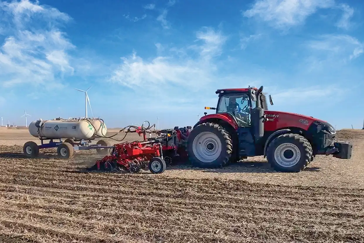 A Case IH 405 Magnum tractor towing a tillage implement and a white dual-tank cart through a harvested field. 