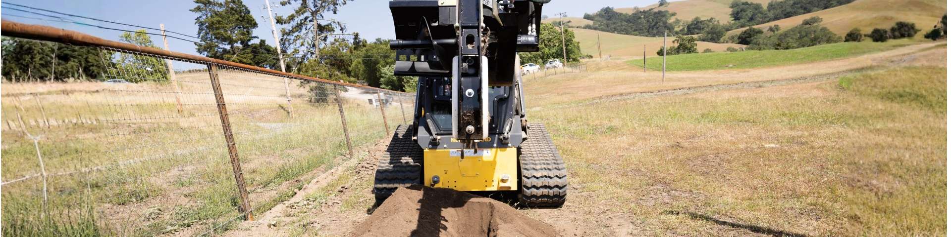 Compact track loader digging trench.