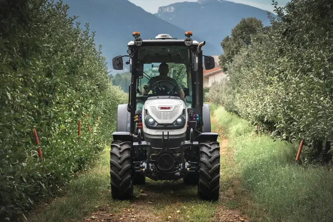 Frontansicht eines STEYR Spezial Obstbautraktors bei der Fahrt durch eine Apfelbaumreihe