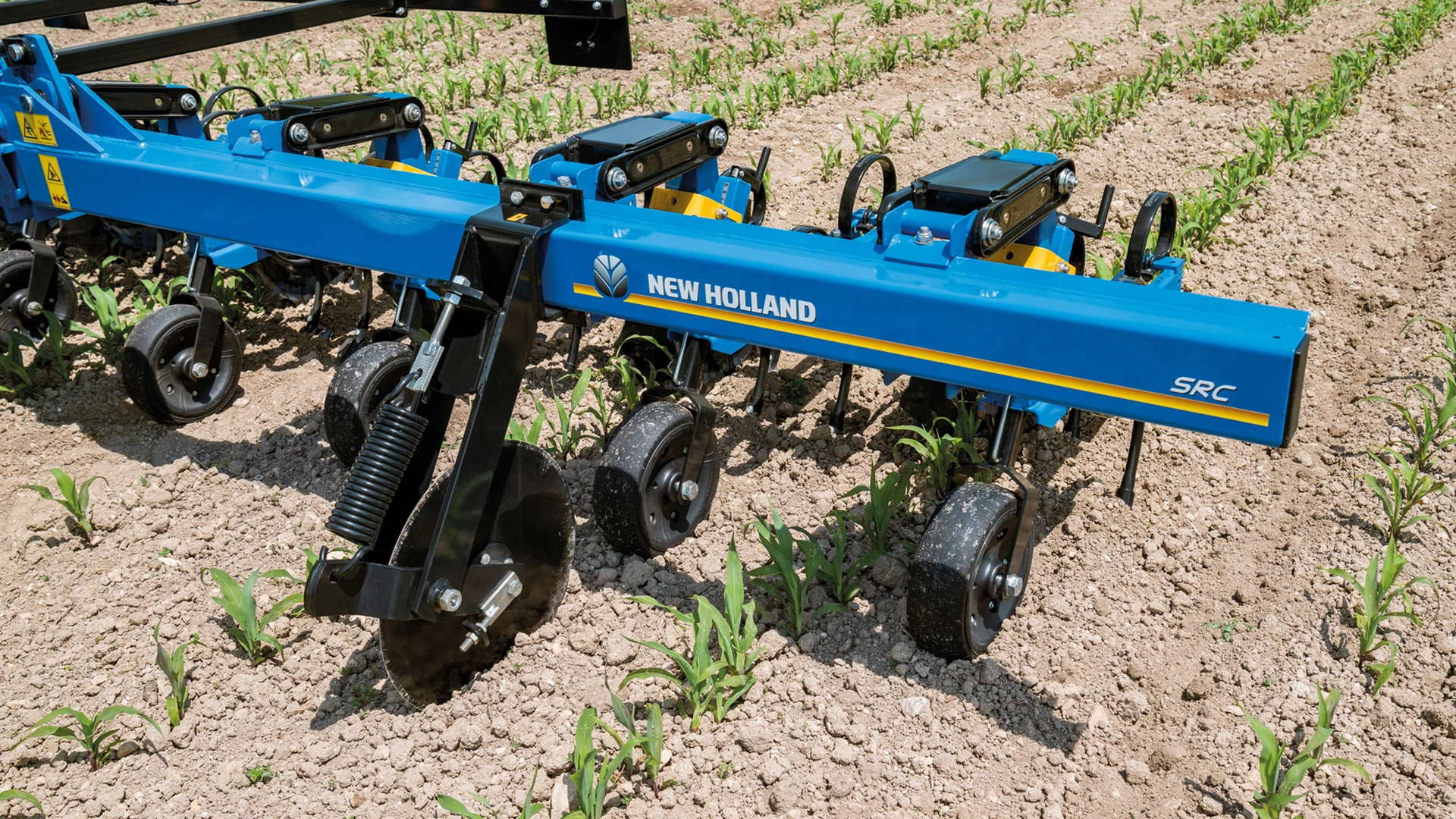 Close shot of New Holland's SRC ＆ SRC SMARTSTEER™ Inter-Row Cultivators, cultivating the soil between green rows on a farm field