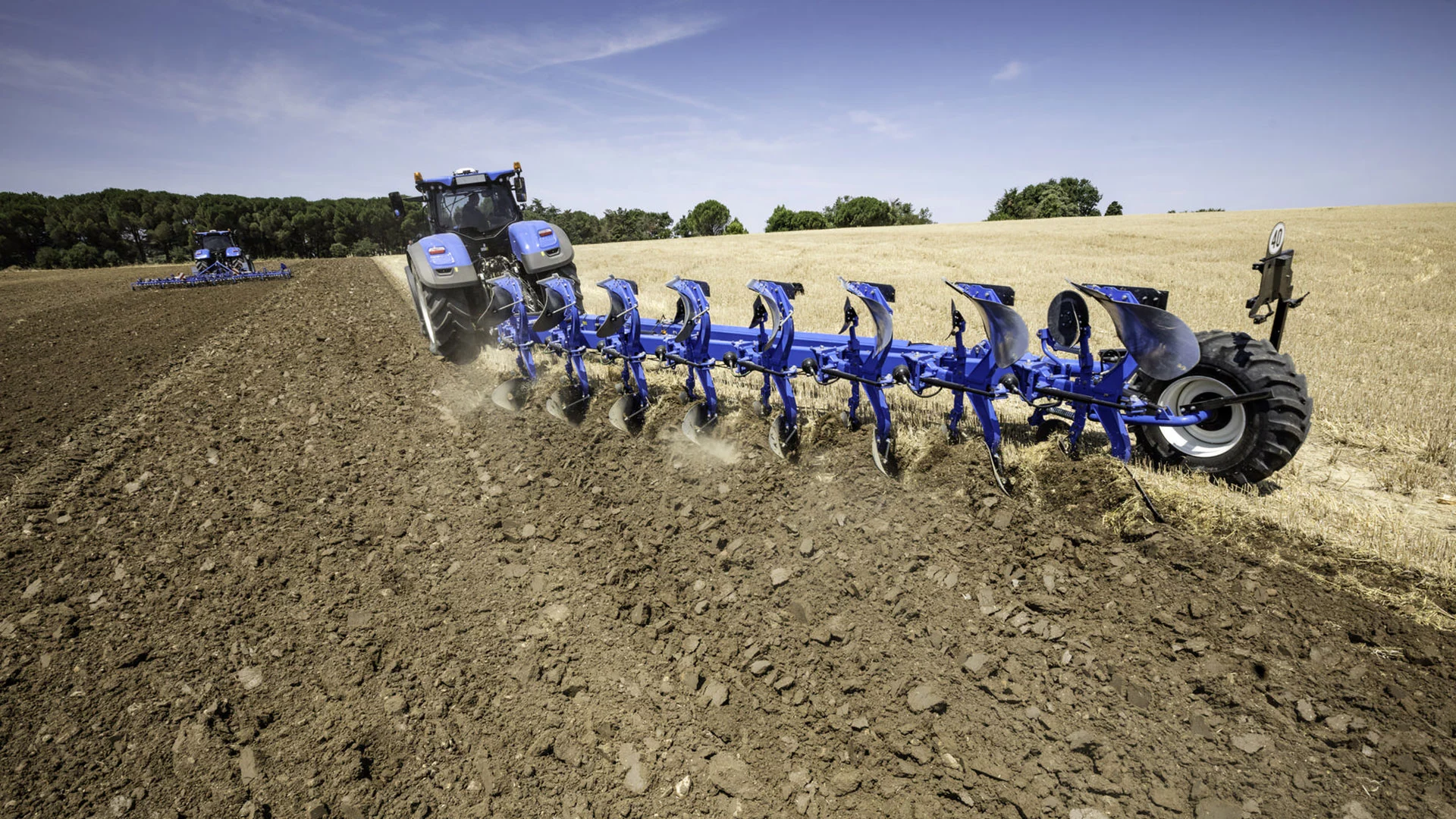 New Holland tractor with a semi mounted agricultural plough working on the field.