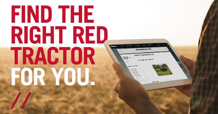 A person in a plaid shirt holds a tablet in a wheat field. On the tablet is a tractor webpage.