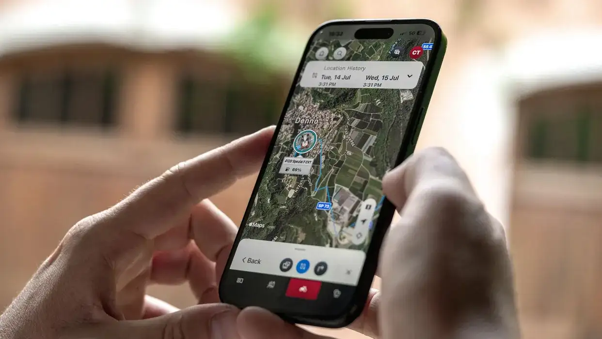 Hand holding a smartphone showing a satellite map with a location-history tracking screen