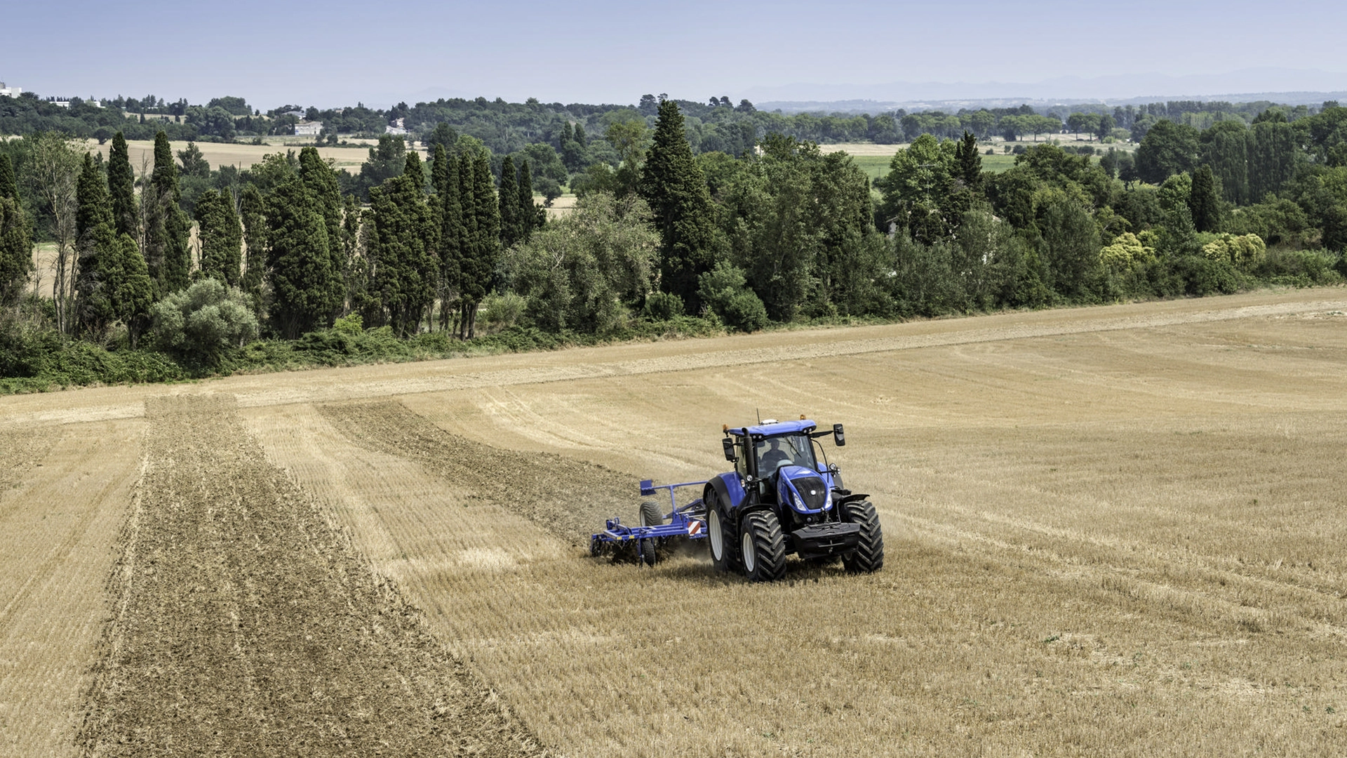New Holland tractor employing a mounted stubble cultivator with Spring Tine Cultivator, discs and rear rollers on the field