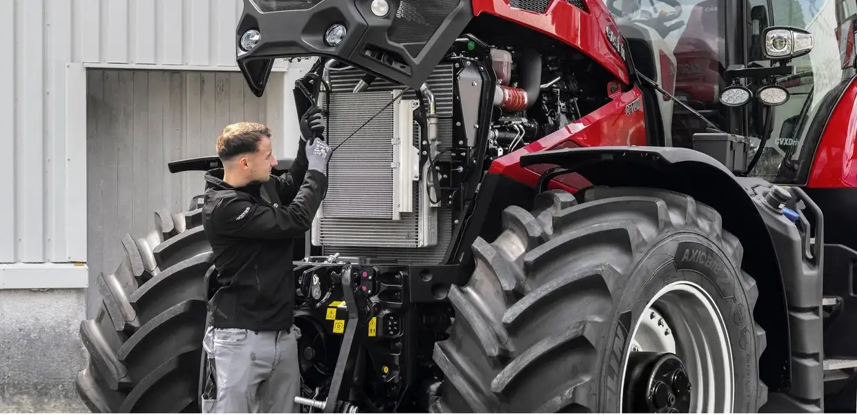 technician stands beside a large red Case IH Optum 440 tractor with the front hood open, inspecting the exposed engine and cooling system outside a workshop.