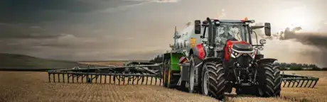 Trattore Case IH rosso al lavoro in un campo di stoppie al tramonto sotto un cielo nuvoloso