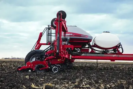 Red Case Ih agricultural planter in a field against a cloudy sky. The machine's large wheels and seed containers are prominent, conveying efficiency and modern farming technology.