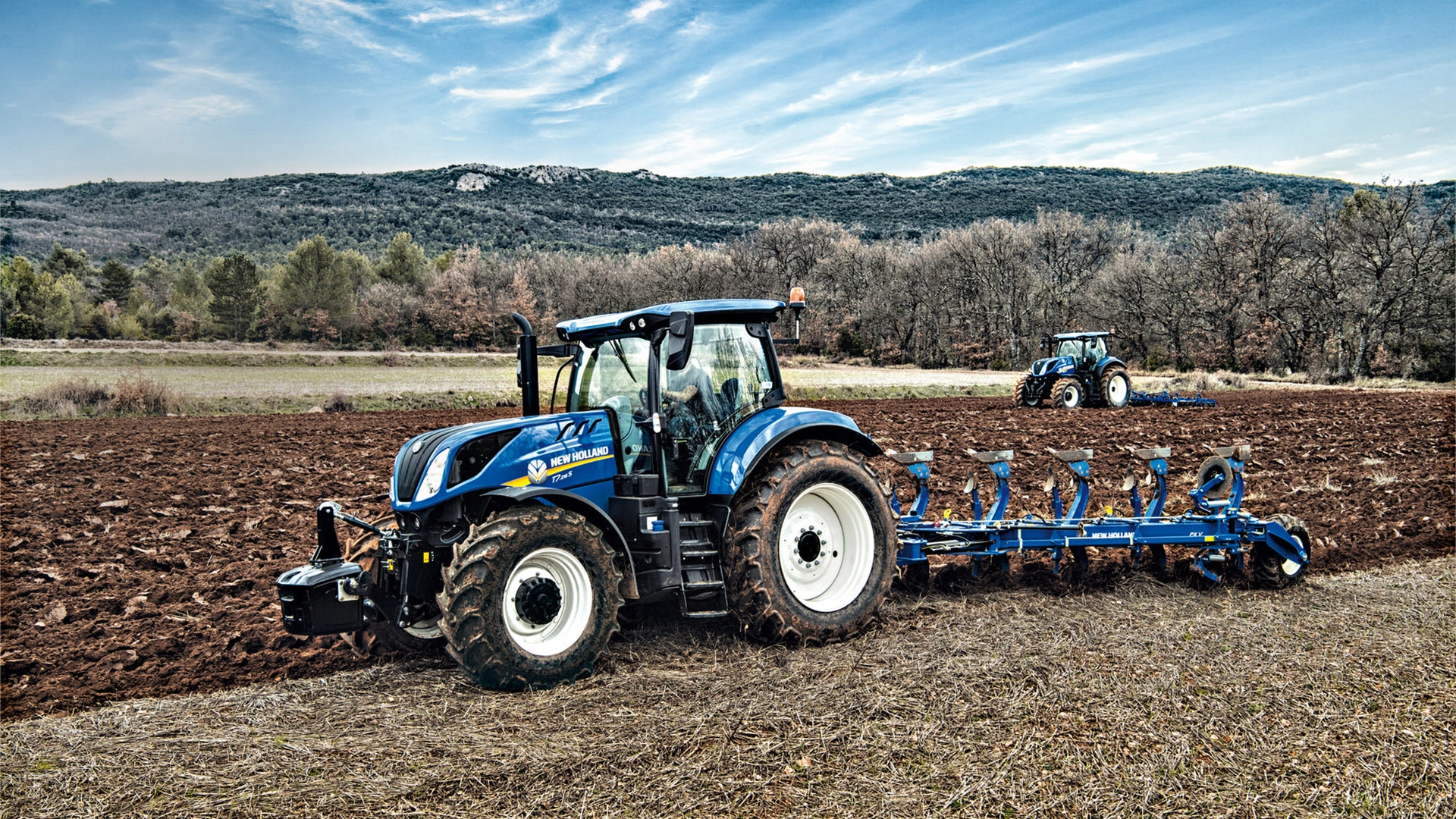 Tractor with a 5 furrow fully-mounted variable width reversible plough working on the field