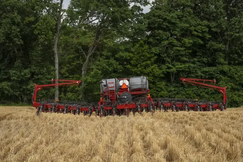 Red Case IH agricultural machinery in a golden wheat field with dense green trees in the background. The scene conveys productivity and the beauty of rural life.