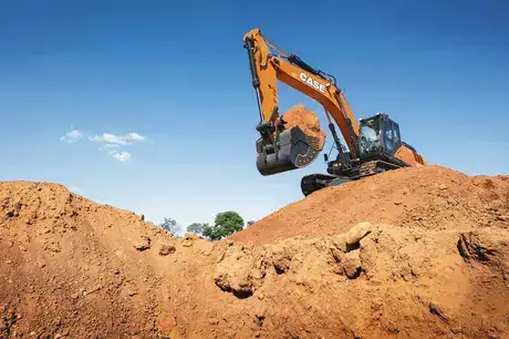 foto ao ar livre da escavadeira hidráulica da Case trabalhando, com destaque para seu guindaste em movimento e a pá cheia de terra.