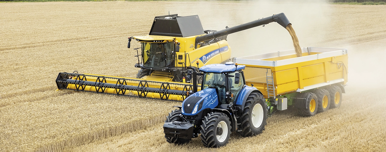 T7 Series tractor pulls a trailer next to a combine