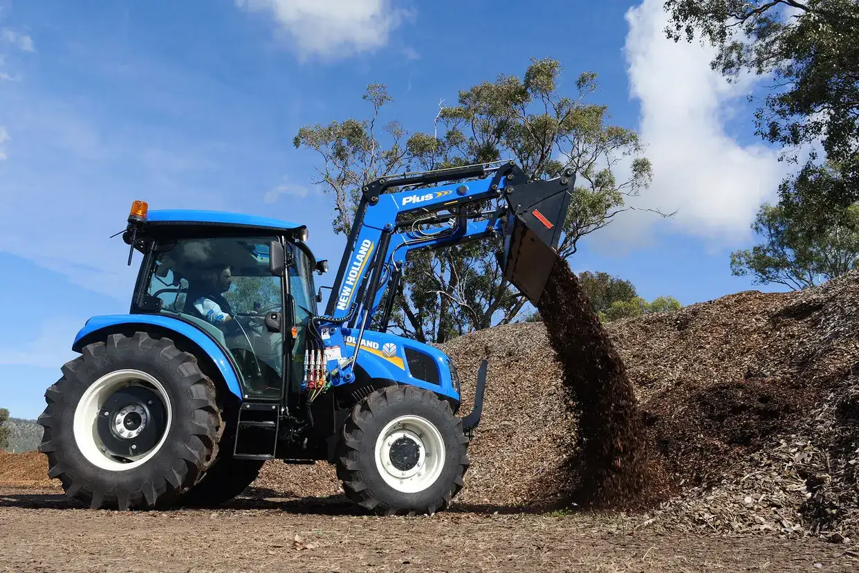 Blue New Holland TT4 Tier 3 tractor in field with loader and 4 in 1 bucket attached