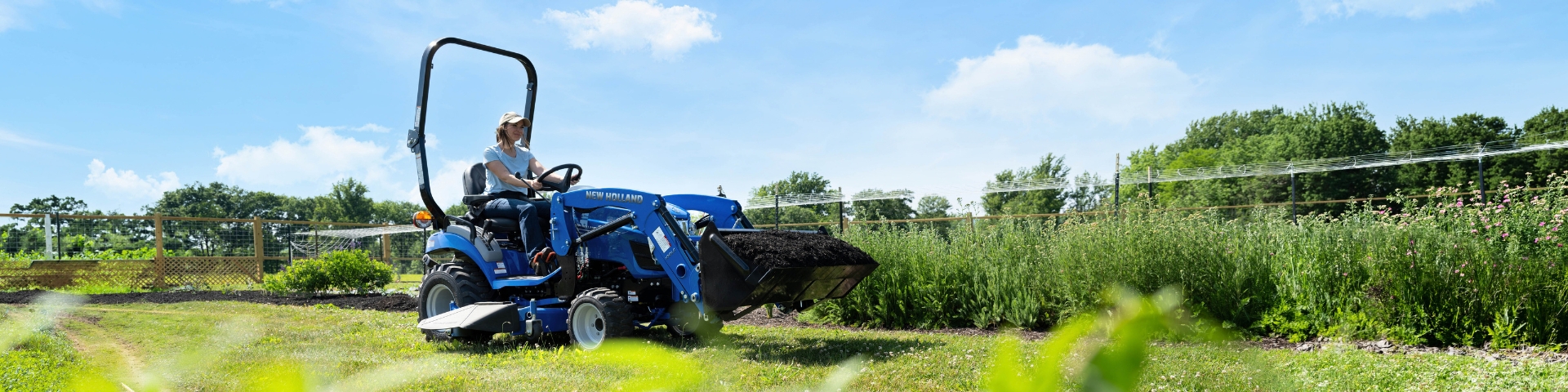 Woman drives a blue tractor in a yard.