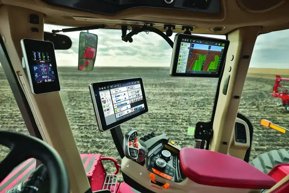 Modern Case IH tractor cabin with digital displays showing controls and maps, overlooking a vast plowed field. The scene is high-tech and functional.