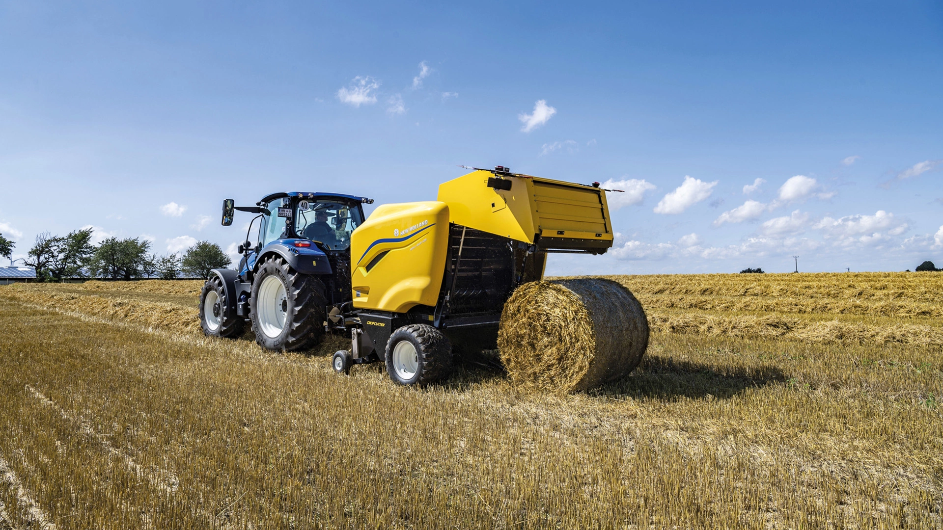 New Holland tractor operating a Roll Baler 125 producing round bale in a field.