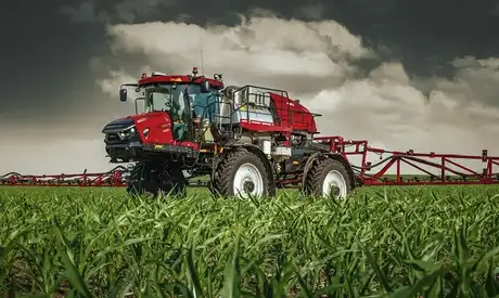 A Case IH Patriot series self-propelled sprayer drives through a field of young green crops its application booms visible in the background.