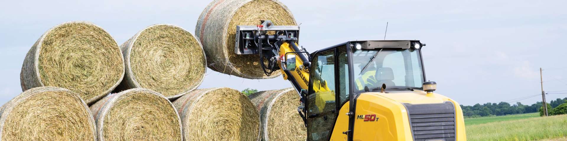 Compact track loader lifting bale of hay.