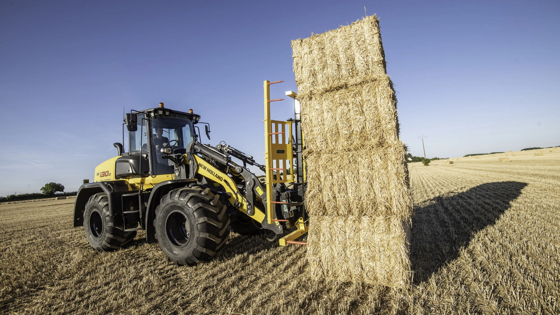 New Holland W130D wheel loader efficiently transporting a towering stack of hay bales .