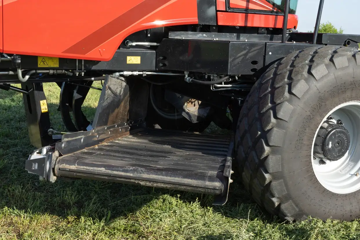Close-up of a Case IH red agricultural machine showing its metal access step, suspension, chassis, and large rugged tire in sunlight.