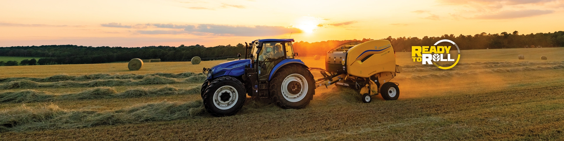New Holland tractor pulls baler in field as the sun is setting.