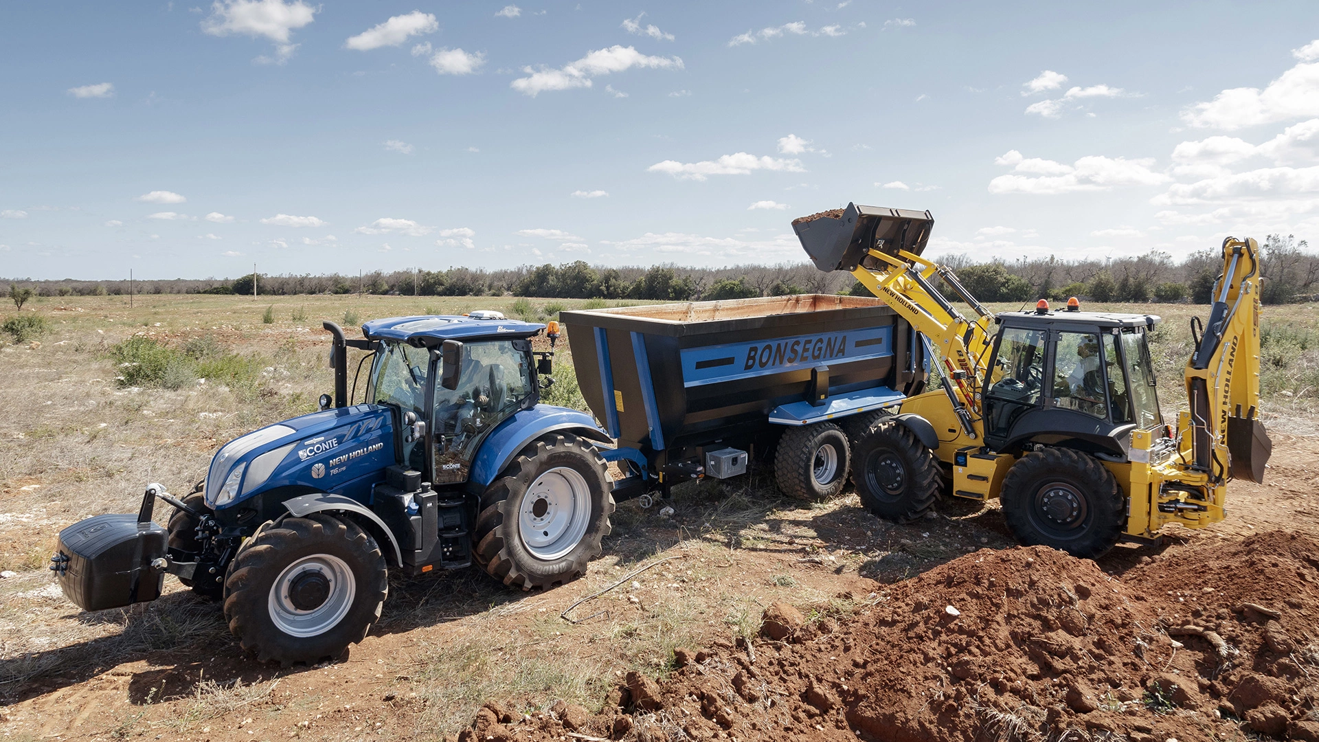 New Holland tractor & backhoe at work, loading soil into a trailer on a clear field day.