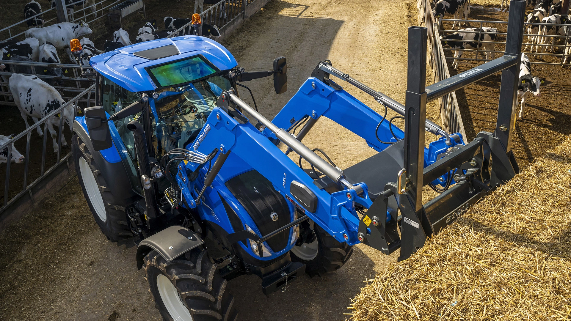 New Holland tractor with loader and fork attachment working at a dairy farm.