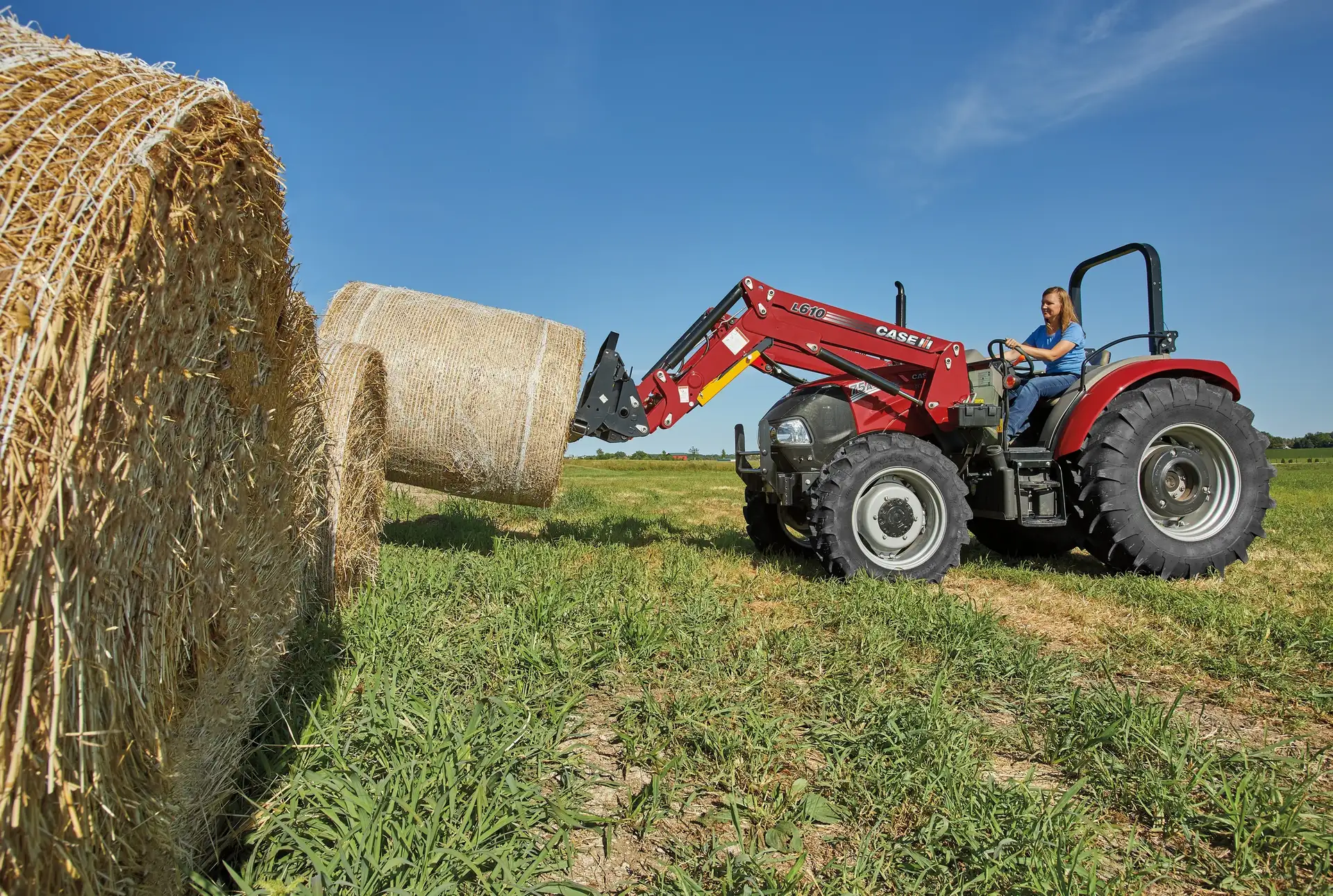 Woman driving a Farmall Utility 75A tractor with L610 Loader with wrapped hay.
