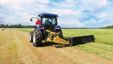 New Holland tractor pulling disc mower in a field.