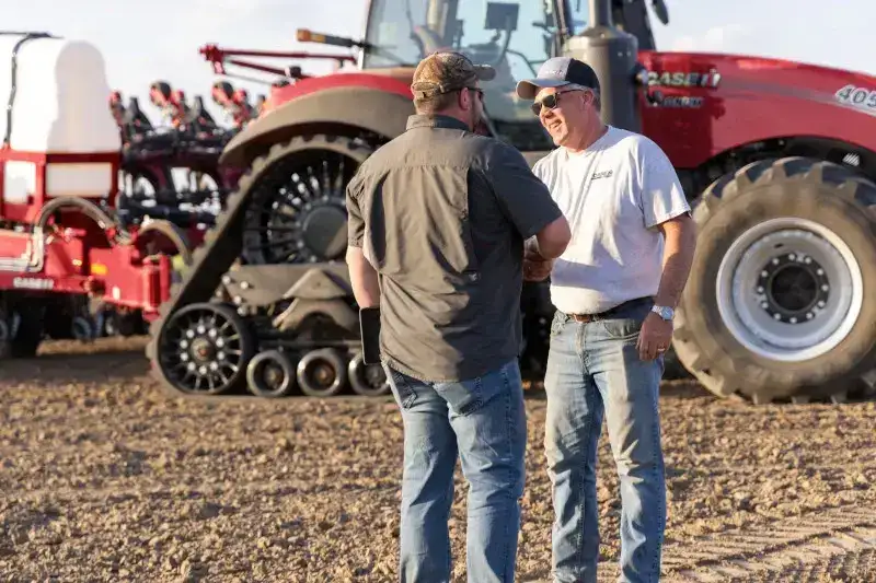 Two men sharing hands in front of a tractor.