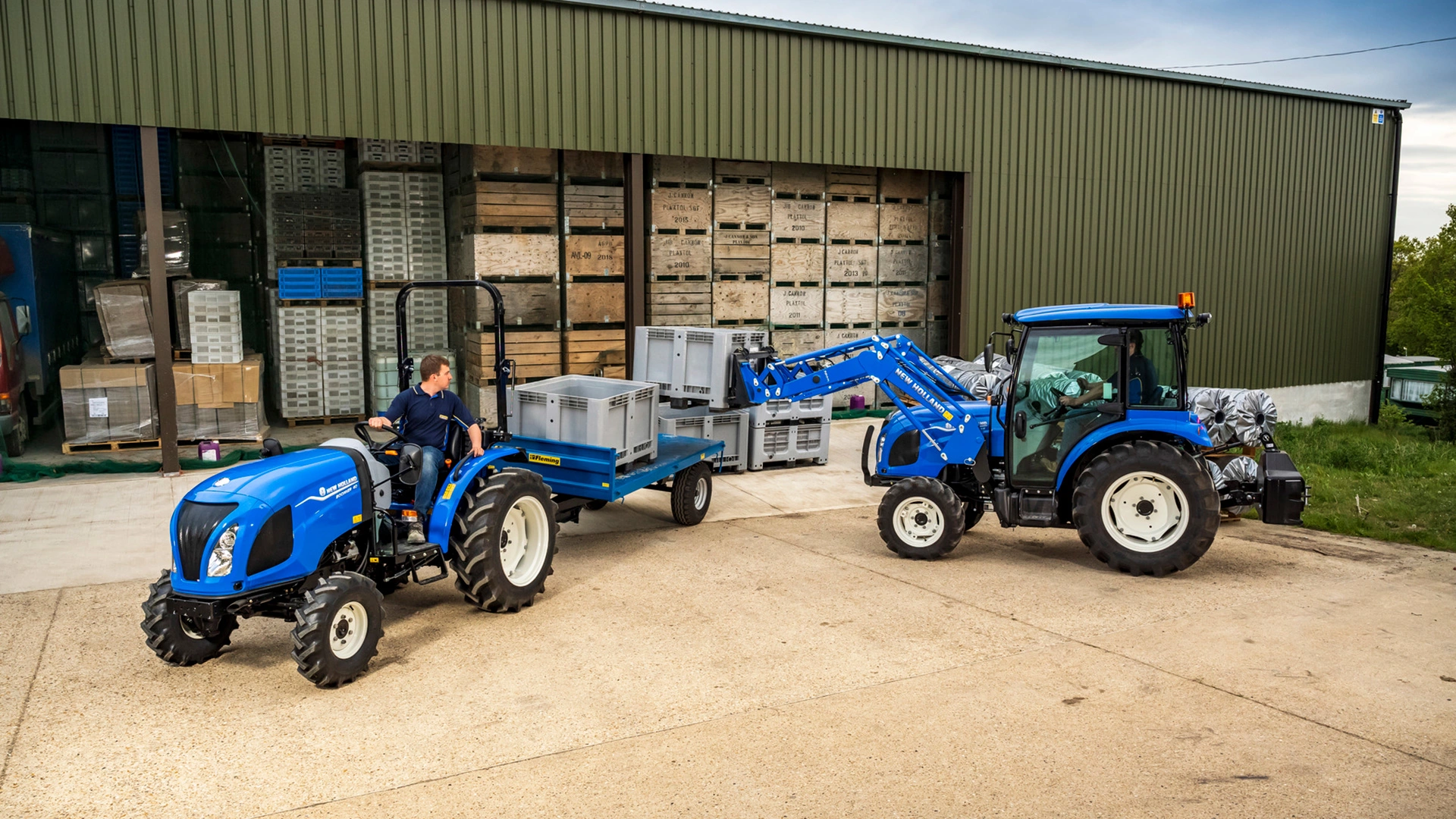 New Holland Boomer tractors with trailer and front loaders moving goods across the farm