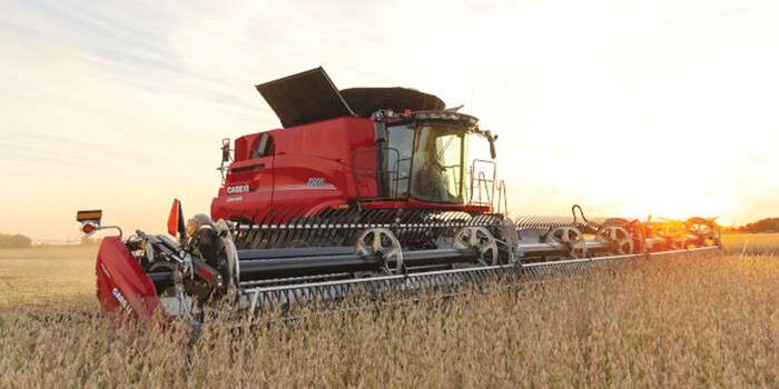 Red Case IH combine harvester working in a golden crop field at sunset under a partly cloudy sky.
