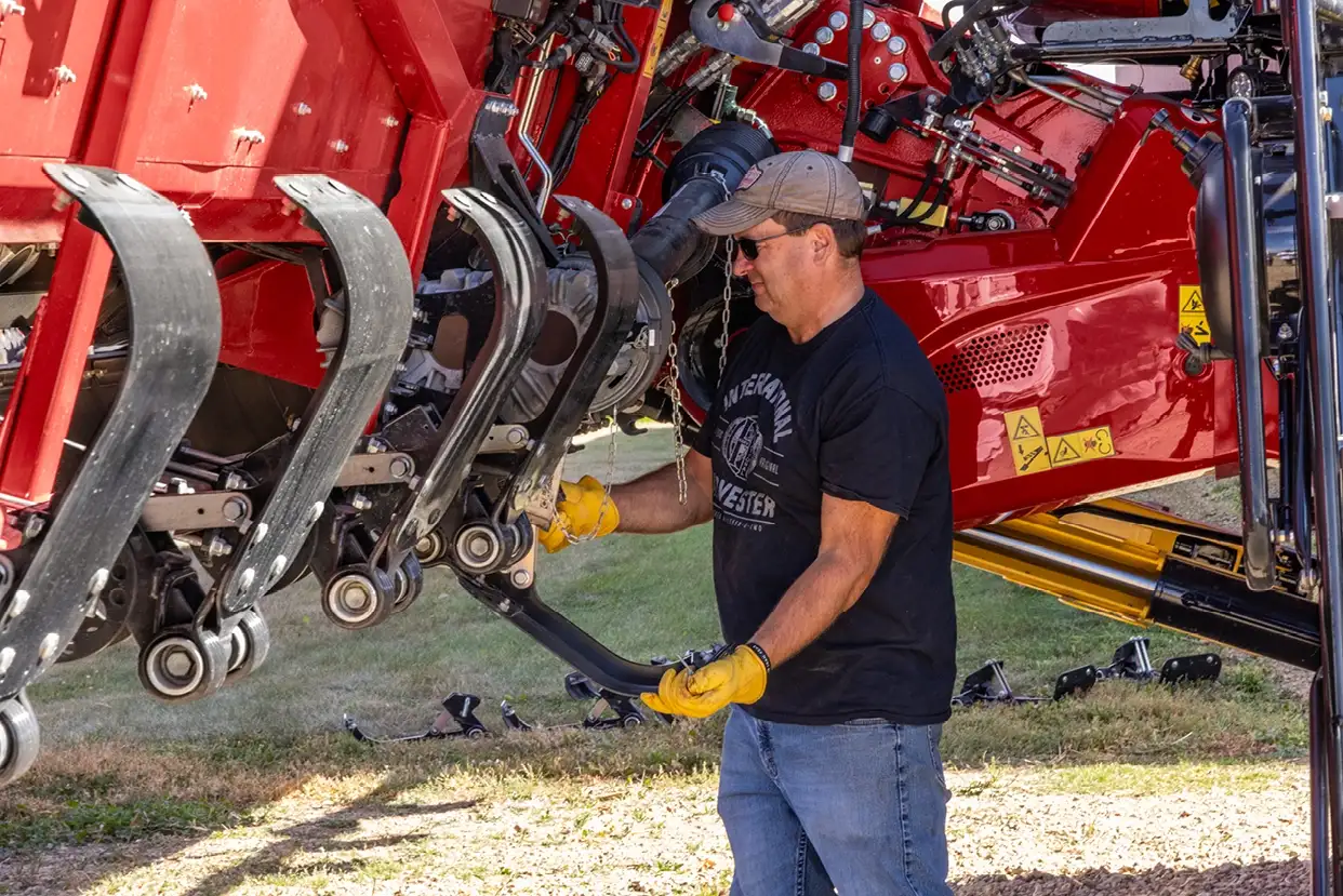A man in a black shirt and yellow gloves inspects a large Case IH C500 series agricultural machine, focusing on its mechanical components.