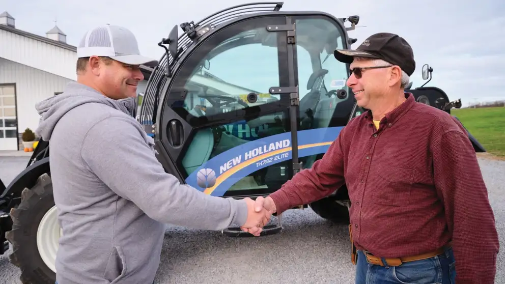 Men shake hands in front of a telehandler