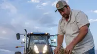 Man handling hay with a tractor behind him.