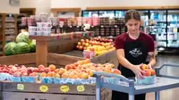 Person stacking fruit in grocery store.